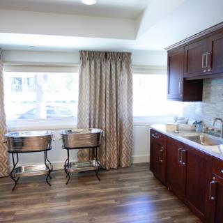A bright kitchen space featuring wooden cabinets, large windows with curtains, and sleek flooring.