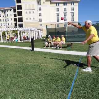 A senior man participating in an outdoor throwing event, while fellow participants watch from a bench.