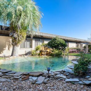 A serene view of a residential pool surrounded by lush greenery and sunny skies.