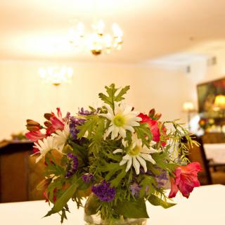 A colorful bouquet of flowers on a dining table in a warmly lit room.