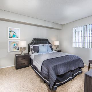 A modern bedroom featuring a neatly made bed with dark bedding, accompanied by two nightstands and soft lighting.