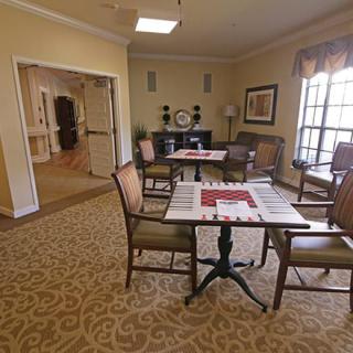 A cozy living area with tables and chairs arranged on a patterned carpet, featuring a large window allowing natural light to enter.