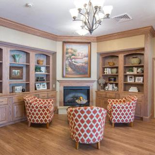 A cozy lounge area featuring patterned chairs, built-in bookshelves, and a warm fireplace.