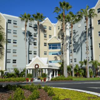 A hotel with palm trees lining the entrance on a sunny day.