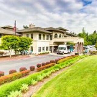 A well-maintained building with manicured landscaping and a vehicle parked in the driveway under a cloudy sky.