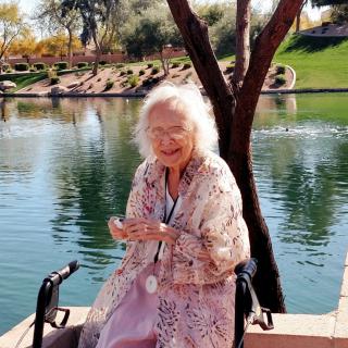 Elderly woman sitting by the lake enjoying a sunny day.