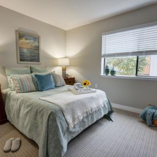 A cozy and well-lit bedroom with a neatly made bed, lamp, and window bringing in natural light.