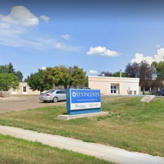 A small commercial building with a sign on the lawn, surrounded by trees and a parked car nearby.