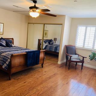 Spacious bedroom with wooden flooring, featuring a bed, ceiling fan, chair, and mirrored closet.