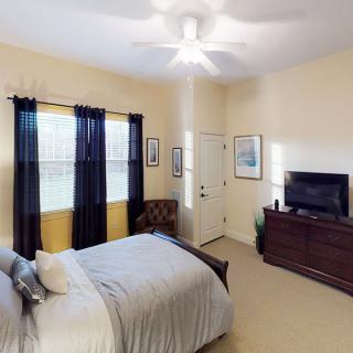 A cozy bedroom with a bed, dresser with a television, and curtains covering the windows.