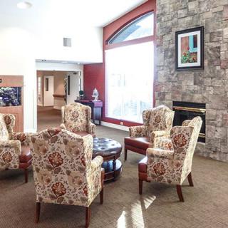 A cozy living room featuring patterned armchairs around a table, a stone fireplace, and a large window.