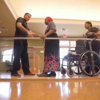 A healthcare professional assists a patient in rehabilitation, while another caregiver stands by with a wheelchair.