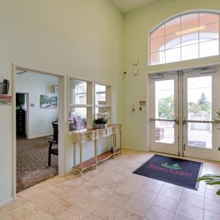 A spacious lobby entrance with large windows and double doors, featuring a decorative table and artwork on the walls.