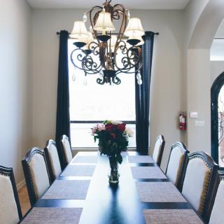 A well-decorated dining room featuring a long table with chairs, a chandelier overhead, and a vase of flowers as the centerpiece.