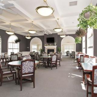 A spacious dining room with elegant decor featuring multiple tables and chairs, large windows, a fireplace, and hanging plants.