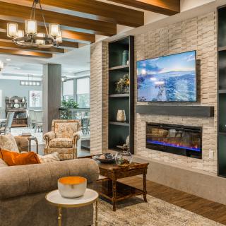 A modern living room featuring a brick wall with a fireplace and mounted television, complemented by stylish furniture and a decorative chandelier.