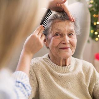 A caregiver combs the hair of an elderly woman, providing home care and comfort.