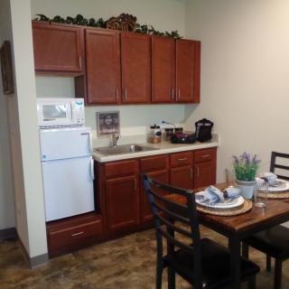 A compact kitchen and dining area with wooden cabinets, a refrigerator, and a table set for two.