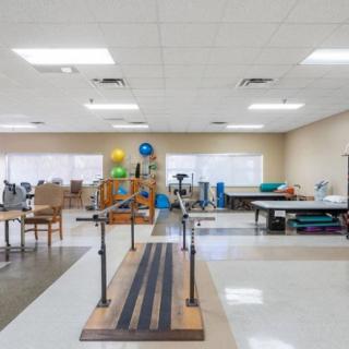 A spacious therapy room equipped with parallel bars and various exercise equipment for rehabilitation and physiotherapy.