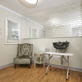 A stylish salon interior featuring a cozy chair, a wash station, and elegant wall tiles.