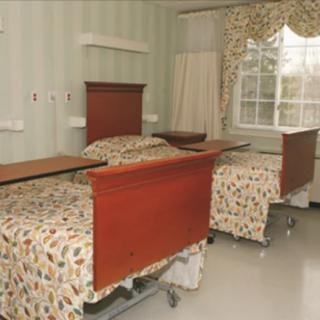 A hospital room with two beds and patterned bedding, featuring a window with drapes.