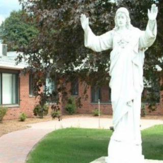 A statue of Jesus with raised arms in an outdoor garden setting.