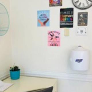 A small office corner with motivational posters, a clock, a desk with a cactus plant, and a hand sanitizer dispenser on the wall.