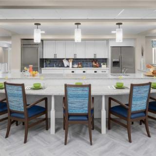 A modern kitchen with a spacious countertop and stylish dining chairs, featuring sleek appliances and pendant lighting.
