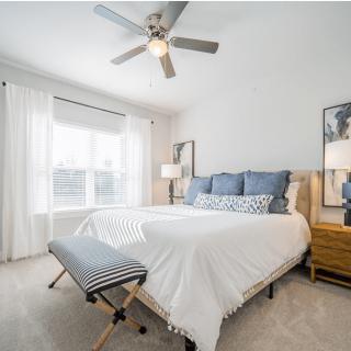 A modern bedroom with neutral tones, featuring a large bed, decorative pillows, and ample natural light.