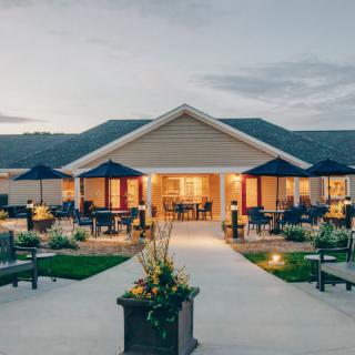 A beautifully lit building with an inviting outdoor patio area, surrounded by well-maintained landscaping and umbrellas, during the evening.