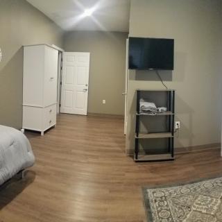 A modern bedroom with a wooden floor, featuring a bed, a white wardrobe, and a wall-mounted TV.