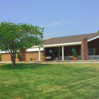 A suburban brick house with a well-maintained lawn and tree in the front yard.