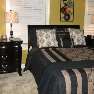 A stylishly furnished bedroom featuring a bed with patterned bedding, matching cushions, and a dark wood nightstand with lamps.