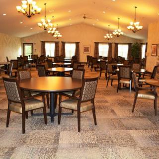An empty dining room with neatly arranged tables and chairs, illuminated by chandeliers.
