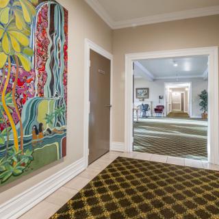 A hallway with colorful artwork on the walls, featuring a patterned carpet and a large mirror.