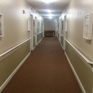 A well-lit corridor with beige walls and carpet, featuring several doors on either side.