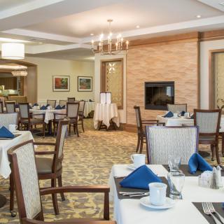 Elegant restaurant dining area with neatly arranged tables and chairs, featuring blue napkins and a chandelier.