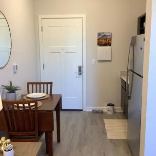 A cozy apartment kitchen with a small dining table and chairs, featuring a refrigerator and a round mirror on the wall.