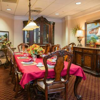 A richly decorated dining room featuring a long table with a red tablecloth, surrounded by wooden chairs and illuminated by a chandelier.