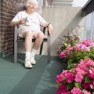 An elderly person relaxing on a balcony surrounded by blooming flowers.