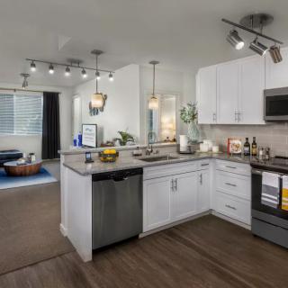 A modern open-concept kitchen with white cabinets, stainless steel appliances, and wood flooring.