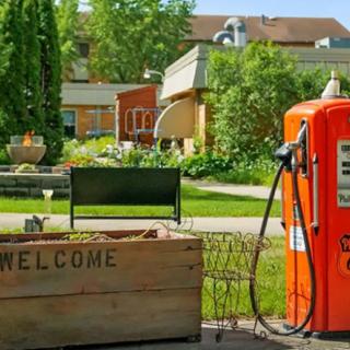 A vintage gas pump stands beside a wooden welcome sign in a picturesque garden setting.