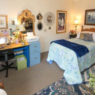 A cozy bedroom with a neatly made bed, a desk area, and various decorative elements on the walls.
