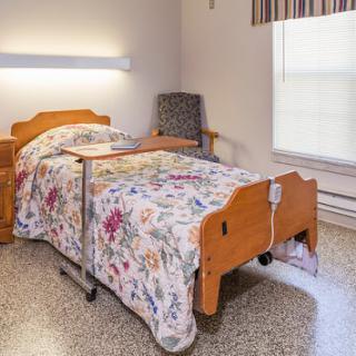 A cozy patient room featuring a hospital bed with floral bedding and a chair.