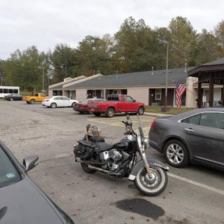 A motorcycle parked in a lot surrounded by various cars and buildings on a cloudy day.