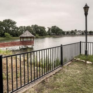 A tranquil lakeside view with a gazebo, fence, and lamp post under a cloudy sky.