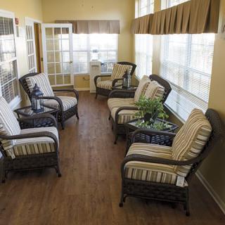A cozy sunroom with wicker chairs and cushions, surrounded by large windows.