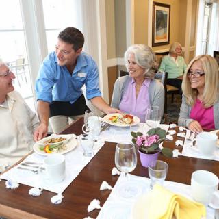 A waiter serves a meal to a group of elderly people enjoying a conversation at a restaurant.