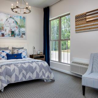 A modern bedroom with stylish decor, featuring a bed with geometric bedding, a large window, and elegant lighting.