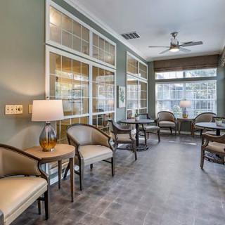 A modern waiting room with chairs arranged around small tables, featuring large windows and soft lighting.